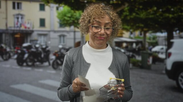 Hispanic woman holding a receipt and a mini shopping cart on a street crosswalk, pursed lips and raised eyebrow indicating doubt; skepticism.