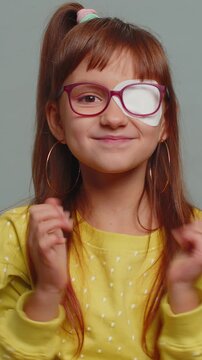 Young preteen child girl kid having protective bandage plaster patch on one eye celebrating success, winning, birthday, lottery jackpot goal achievement. Toddler children isolated on gray background