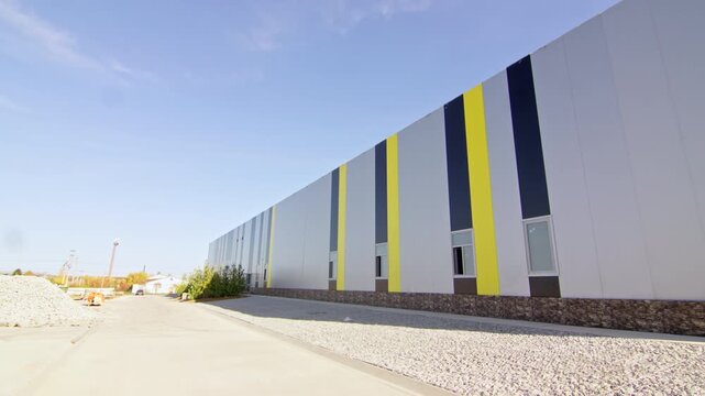 Modern commercial warehouse stretches under clear sky on bright sunny day. Spacious property layout offers efficient access for logistics