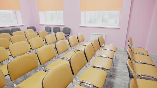 Chairs with metal legs create cozy seating layout for large audience. Orderly hall setup offers calm atmosphere for corporate sessions