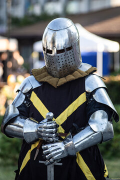Medieval knight wearing full plate armor and helmet, standing outdoors with a sword in his hands. Historical reenactment of a medieval warrior representing chivalry, medieval warfare, European history