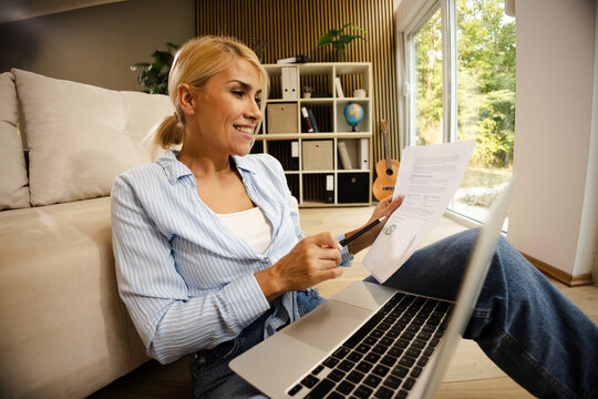 Woman Works on Documents in a Small Office Space While Sitting on the Floor With a Laptop