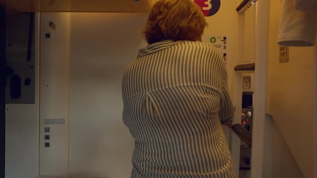 Senior woman enters modern train compartment and closes door for privacy. Elderly passenger settles inside sleeper car cabin during railway travel. Comfortable journey for active pensioner.