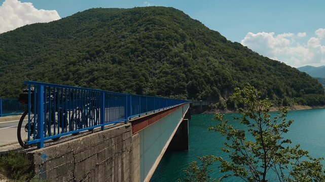 Two loaded touring bicycles parked on a bridge over Piva Lake in Montenegro. Turquoise water and forested mountains create a scenic travel landscape