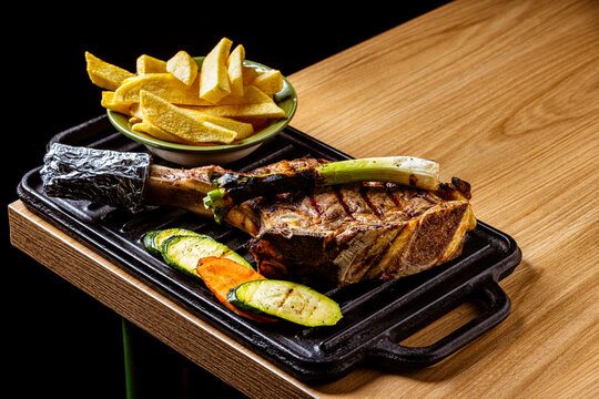 Grilled Tomahawk Ribeye Steak Served on Cast Iron Skillet with French Fries, Grilled Vegetables, and Scallion