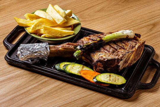 Grilled Tomahawk Ribeye Steak Served on Cast Iron Skillet with French Fries, Grilled Vegetables, and Scallion