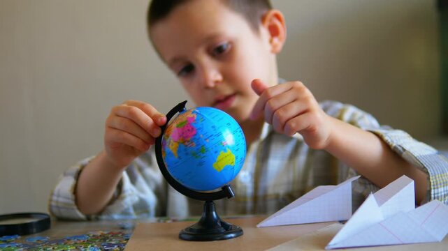 Curious young boy spinning a small world globe while studying geography and exploring the planet