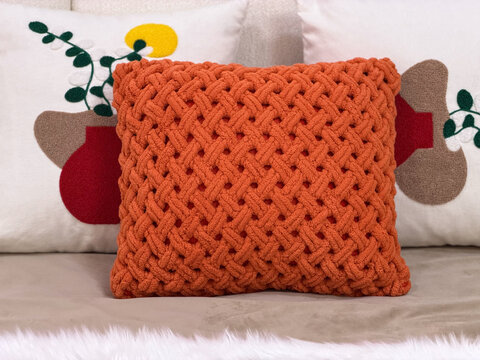 Cozy modern sofa styled with a chunky knitted orange cushion and decorative pillows, warm contemporary home interior with textured textiles.