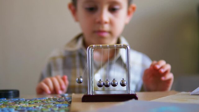 Curious boy learning about momentum physics by releasing a swinging Newton's Cradle