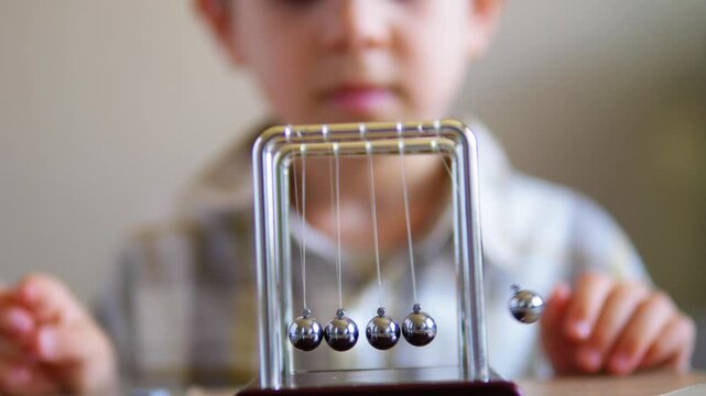 Curious boy learning physics by playing with a swinging Newton's Cradle desk toy