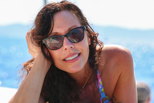Close‑up portrait of a woman wearing sunglasses aboard a sailboat near Milos, her relaxed expression reflecting the warmth and serenity of Mediterranean summer travel.