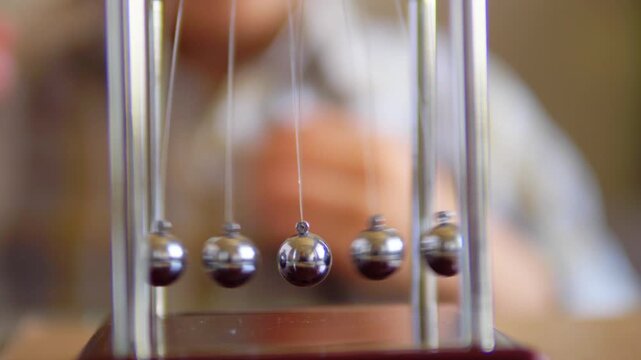 Cinematic close up of kinetic pendulum motion as a child's hands pull back opposing metallic spheres on a Newton's cradle