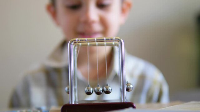 boy watching a swinging Newton's cradle with fascination while learning about physics
