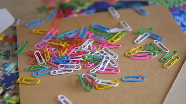 Colorful Paperclips Falling and Scattering on a Messy Brown Desk with Puzzle Pieces