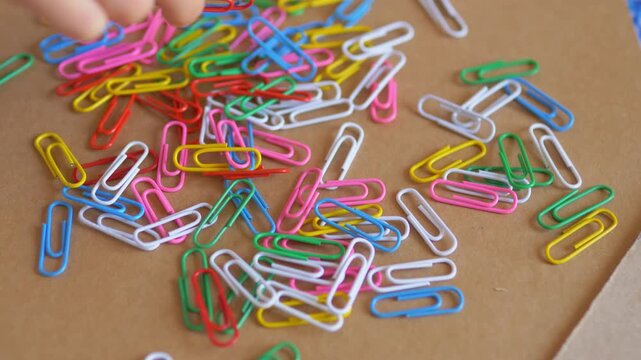 Child's hand touching and sorting a scattered pile of brightly colored paperclips on a desk