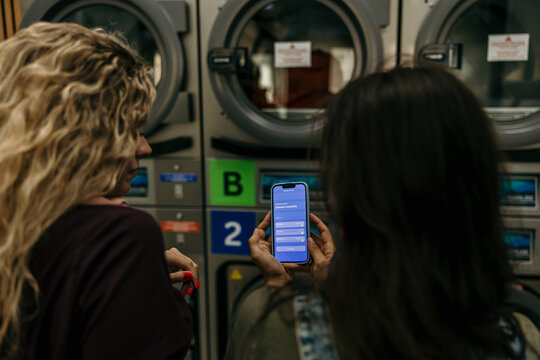 Women using smartphone app for laundry at laundromat