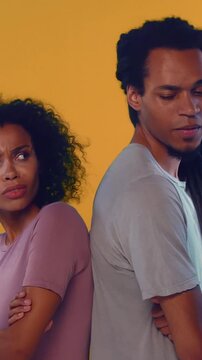 Young African American man and woman stand back to back with crossed arms looking angry and resentful. Couple avoids eye contact after conflict or argument while posing in studio setting.
