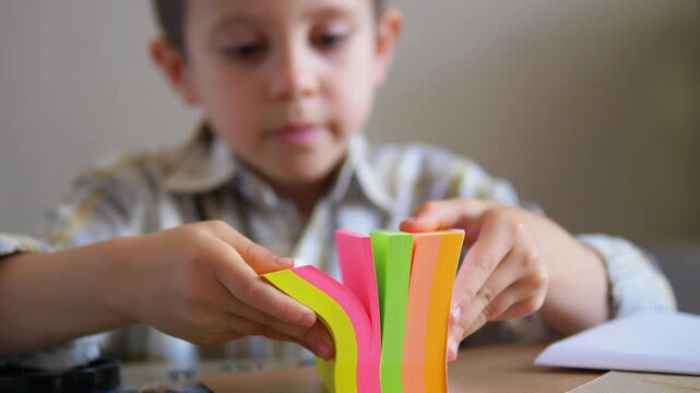 young boy fanning and playing with a bright multi-colored block of sticky notes