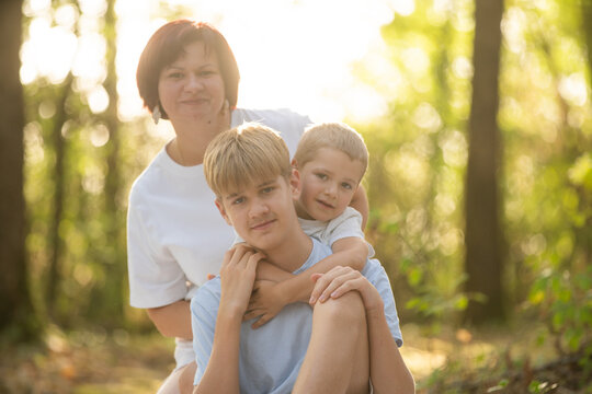 Mother embracing sons in a warm summer forest, showing love, care, and family bond during golden hour