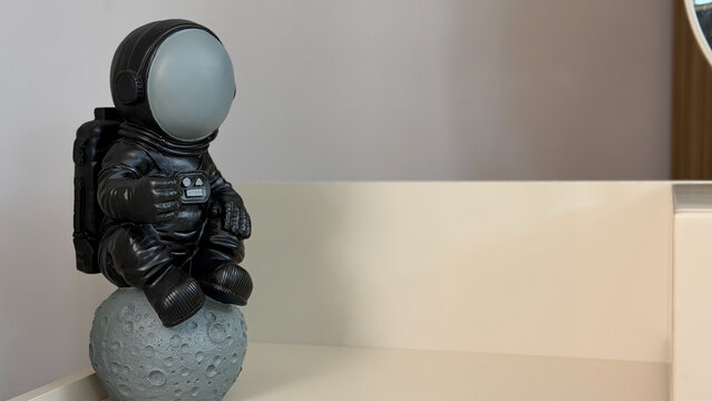 Decorative astronaut figurine sitting on a moon model in a modern interior, space exploration concept with copy space.