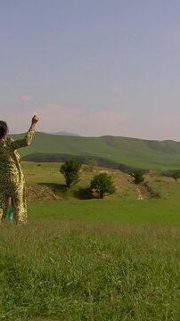 A mother and her little daughter in a white dress watching a colorful kite fly high in the blue sky on a green hill, slow motion vertical video.