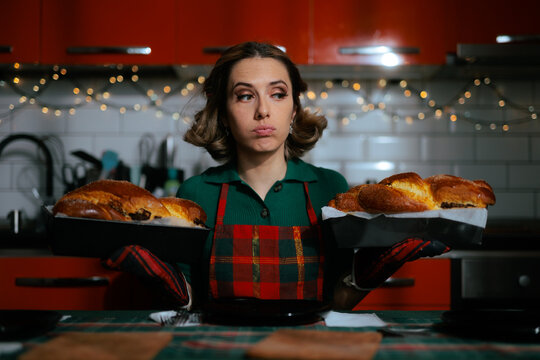 Disappointed Housewife Holding Trays With Baked Christmas Sweet Bread. Puzzled young woman wearing plaid apron looking at burned or failed traditional cozonac