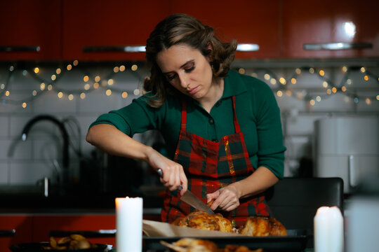 Housewife Carving Roasted Christmas Chicken At Decorated Kitchen Counter. Focused woman using knife to cut holiday poultry near candle light