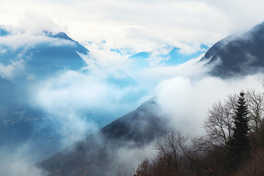 Clouds over the Como lake and autumn Alps mountains. Como, Italy. Beautiful autumn landscape at foggy morning