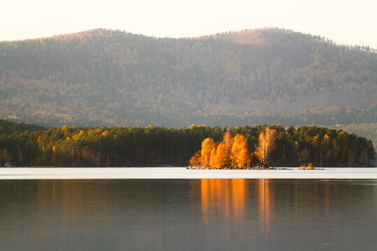Lake in the mountains at sunset. Autumn mountains with yellow and green trees are reflected in the water. Turgoyak lake in Southern Urals, Russia.