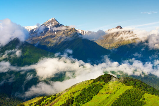 Morning fog in the mountains at sunrise. Ingushetia, North Caucasus, Russia. White clouds over the green mountains and hills.