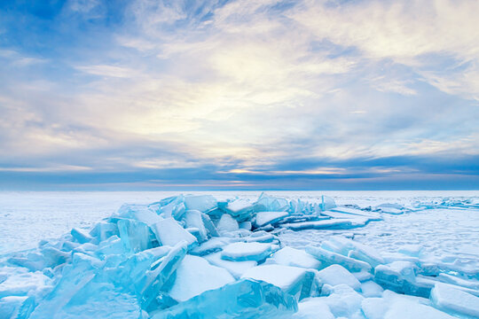 Ice floes with snow on Baikal lake in winter. Blue sky with clouds at sunrise. Olkhon island, Baikal, Siberia, Russia.