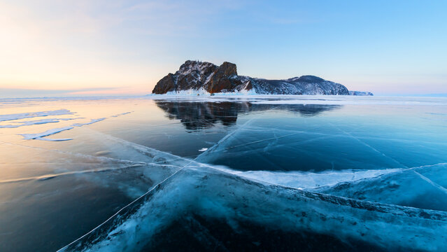 Blue transparent cracked ice on Baikal lake in winter. Khoboy cape of Olkhon island, Baikal, Russia. Winter landscape at sunrise