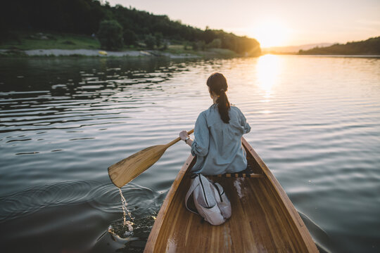Woman paddling canoe on calm lake at sunset