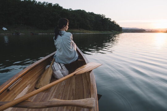 Woman relaxing in canoe on peaceful lake at sunset