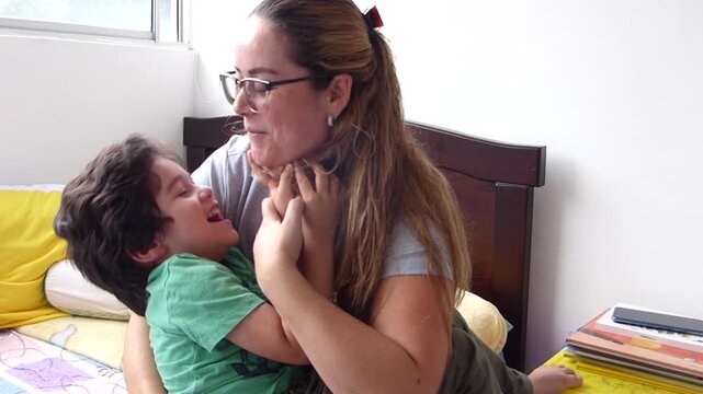 Happy mother laughing and playing with her joyful young son lying on a bed sharing a fun and affectionate moment together at home