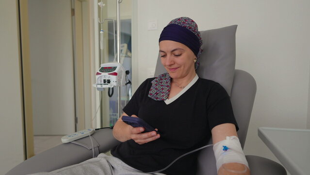 Cancer patient using smartphone during chemotherapy treatment in oncology clinic, healthcare recovery setting illustrating resilience, connection, support and healing