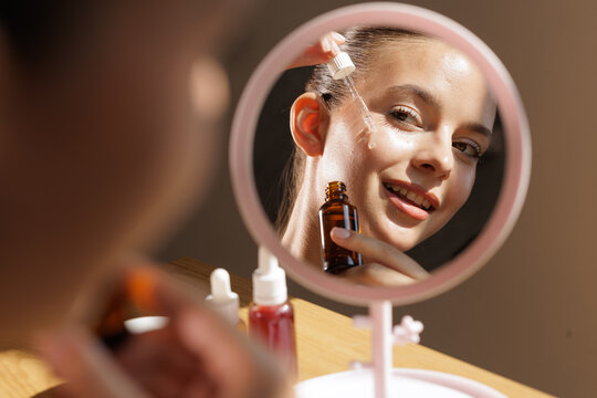 Woman Applying Facial Serum in Mirror Reflection