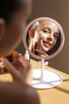 Woman Applying Facial Serum in Front of Mirror