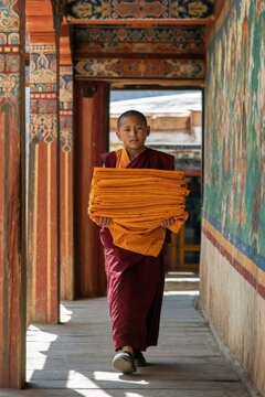 Buddhist monk carrying folded saffron robes through a richly painted monastery corridor in Bhutan. Spiritual tradition, religious service, cultural heritage, and monastic life.