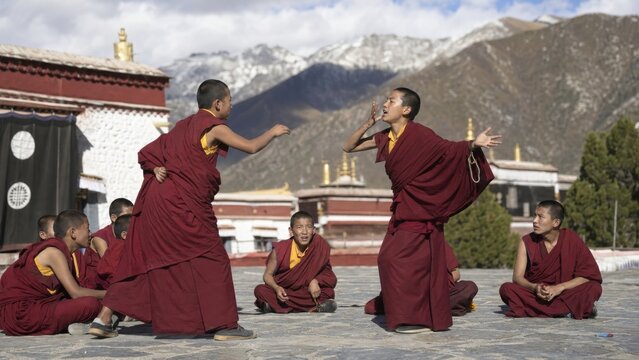 Buddhist monks debating in a Tibetan monastery courtyard. Traditional monastic education, spiritual practice, cultural heritage, and Himalayan mountain landscape.