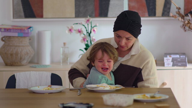 Mother comforting crying toddler at dining table in family home during cancer recovery, highlighting maternal care, emotional support, attachment, resilience and family connection