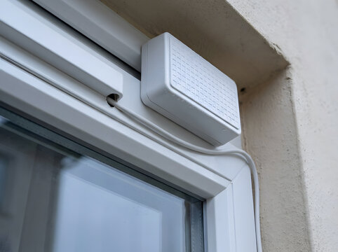 Smart home security sensor on window frame | Outdoor wireless alarm system component | White magnetic contact sensor for home safety | Intruder detection device on white PVC window