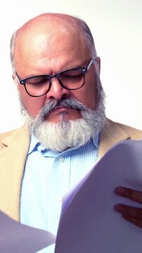 Indian Asian senior businessman with beard in a suit and spectacles ,standing and reviewing business documents, looking worried or disappointed, isolated on a white background