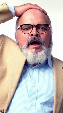 Indian Asian elderly businessman with a beard, wearing a suit, standing on a white background, showing a shocked or distressed expression with wide eyes and open hands