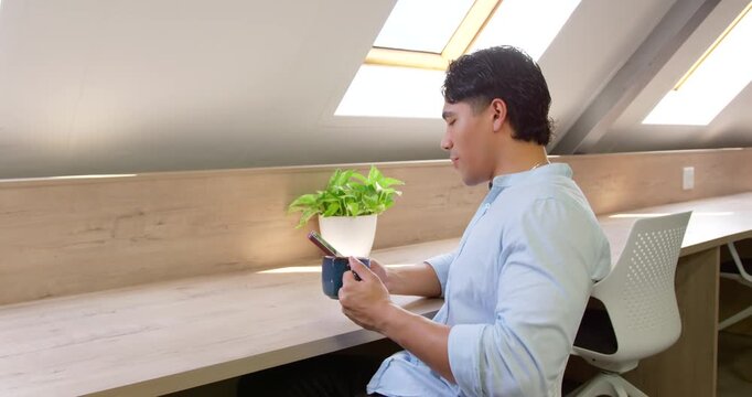 Man sitting at home office under skylight, resting phone over mug, checking texts, copy space