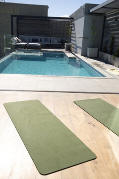Rectangular pool is reflecting pergola shadows on clear water, olive-green mats on rooftop deck