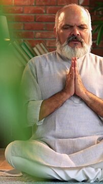 Indian senior man sitting peacefully on the floor in traditional kurta pyjama, practicing deep breathing, yoga, or meditation at his modern home