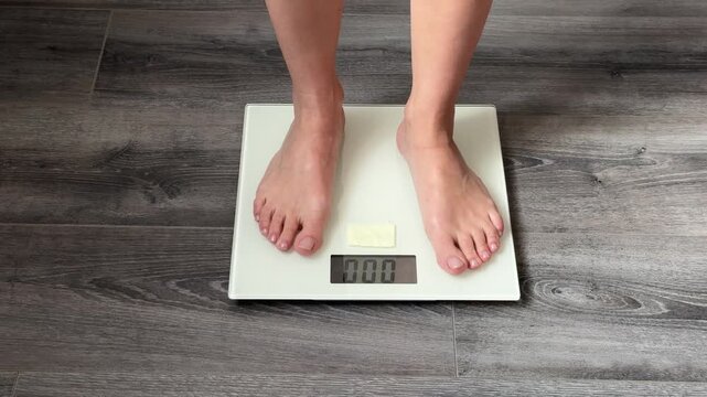 A young woman steps onto a white scale to weigh herself.