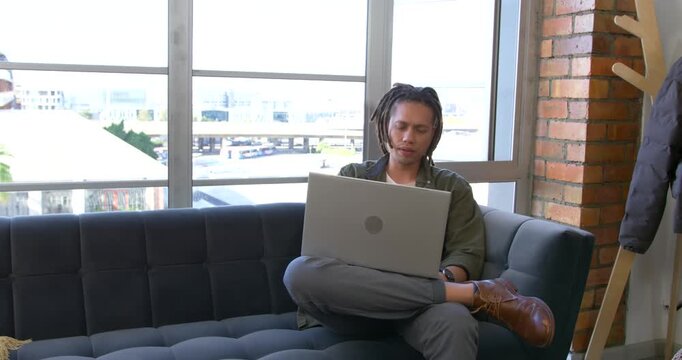 African American man sitting on sofa, glancing at traffic, returning to laptop, working, copy space