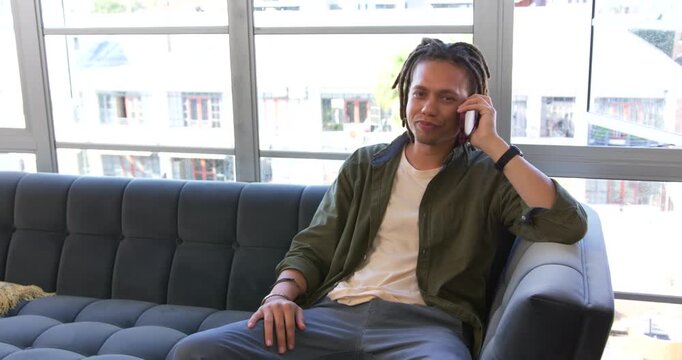 Receiving call, African American man seated on sofa by window, catching up on phone, copy space